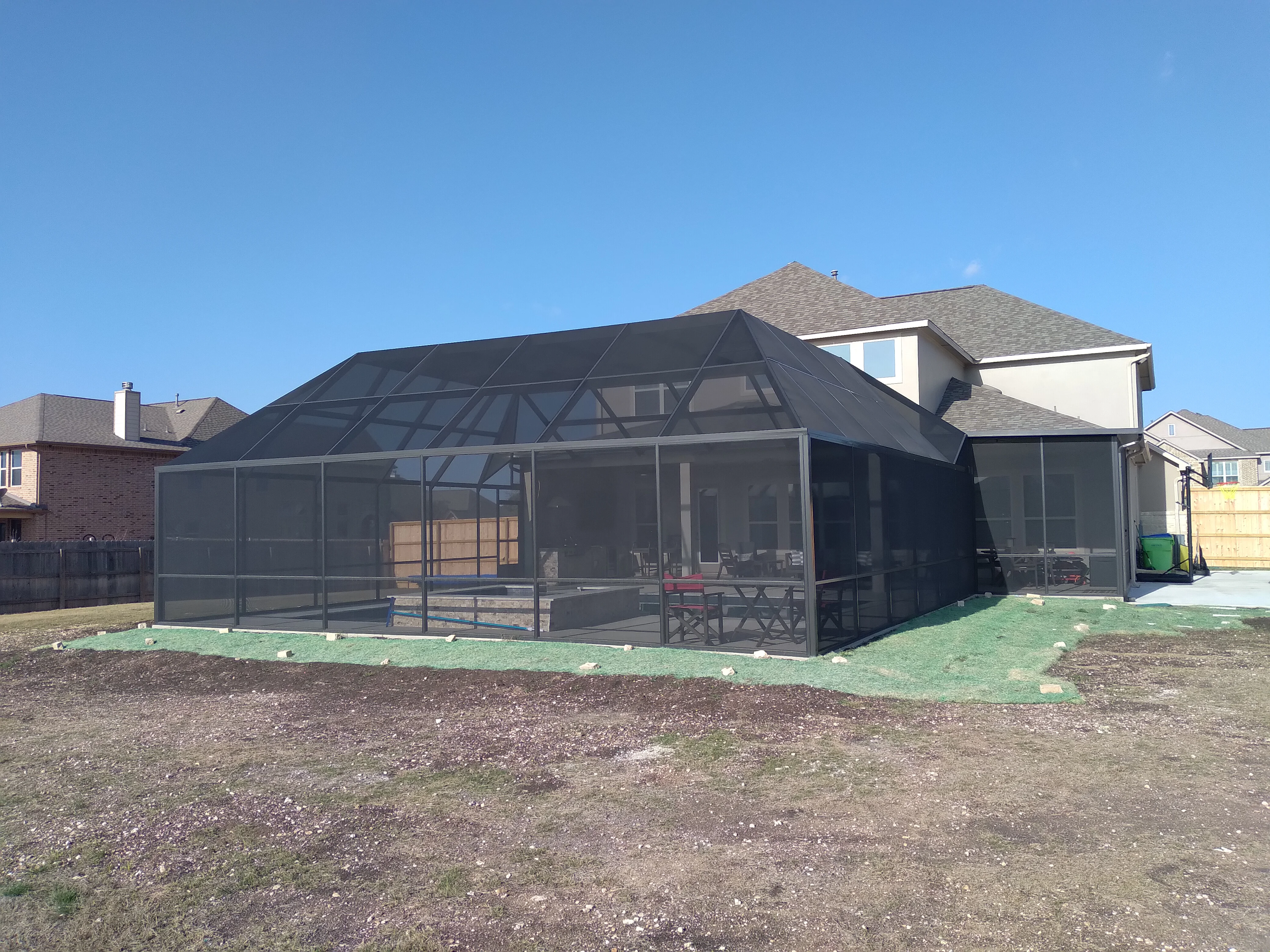 Black aluminum pool enclosure with mesh screening and peaked roof on residential property
