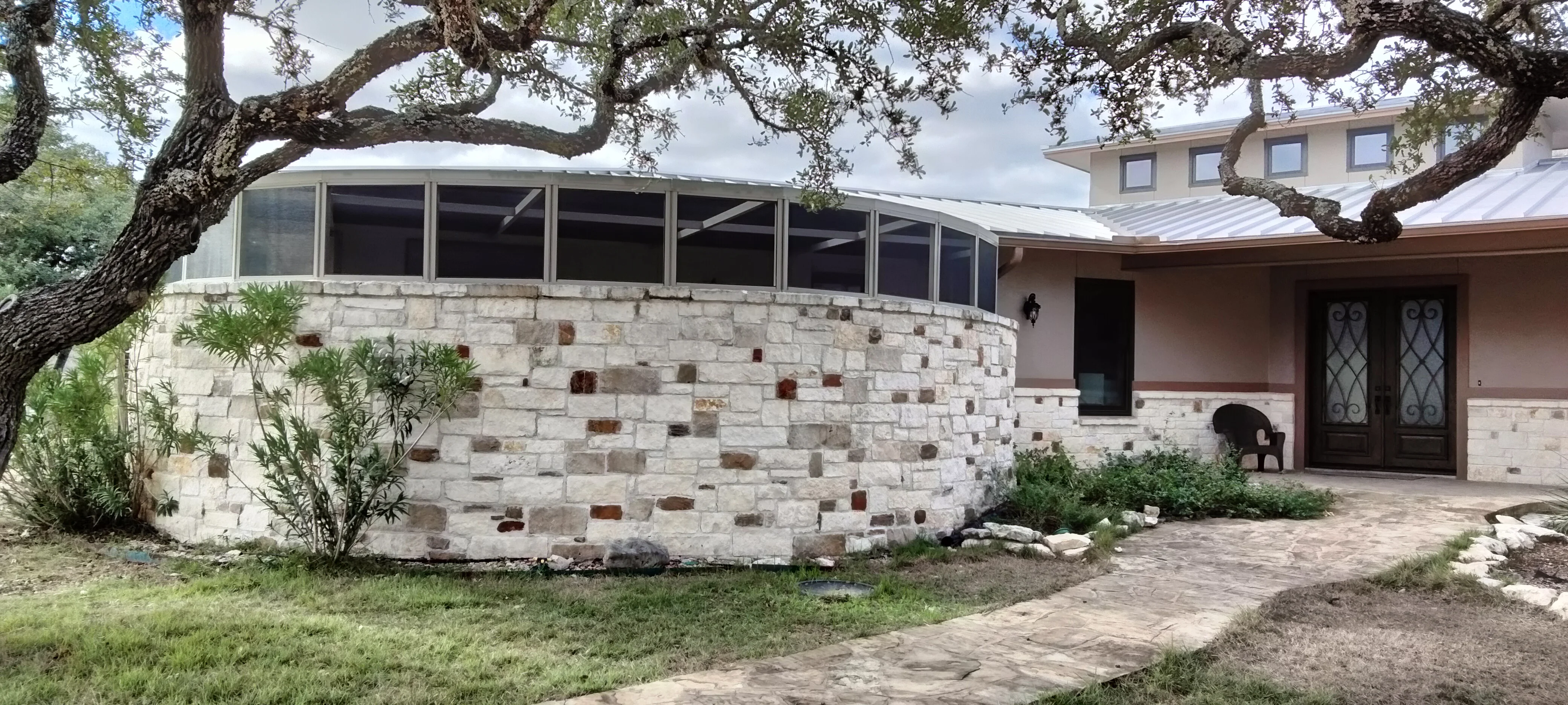 Curved stone patio enclosure with metal-frame windows and stacked stone veneer walls
