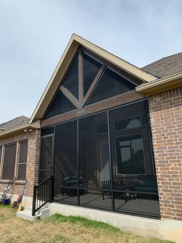 Screened patio enclosure with gabled roof and black aluminum frame on brick home