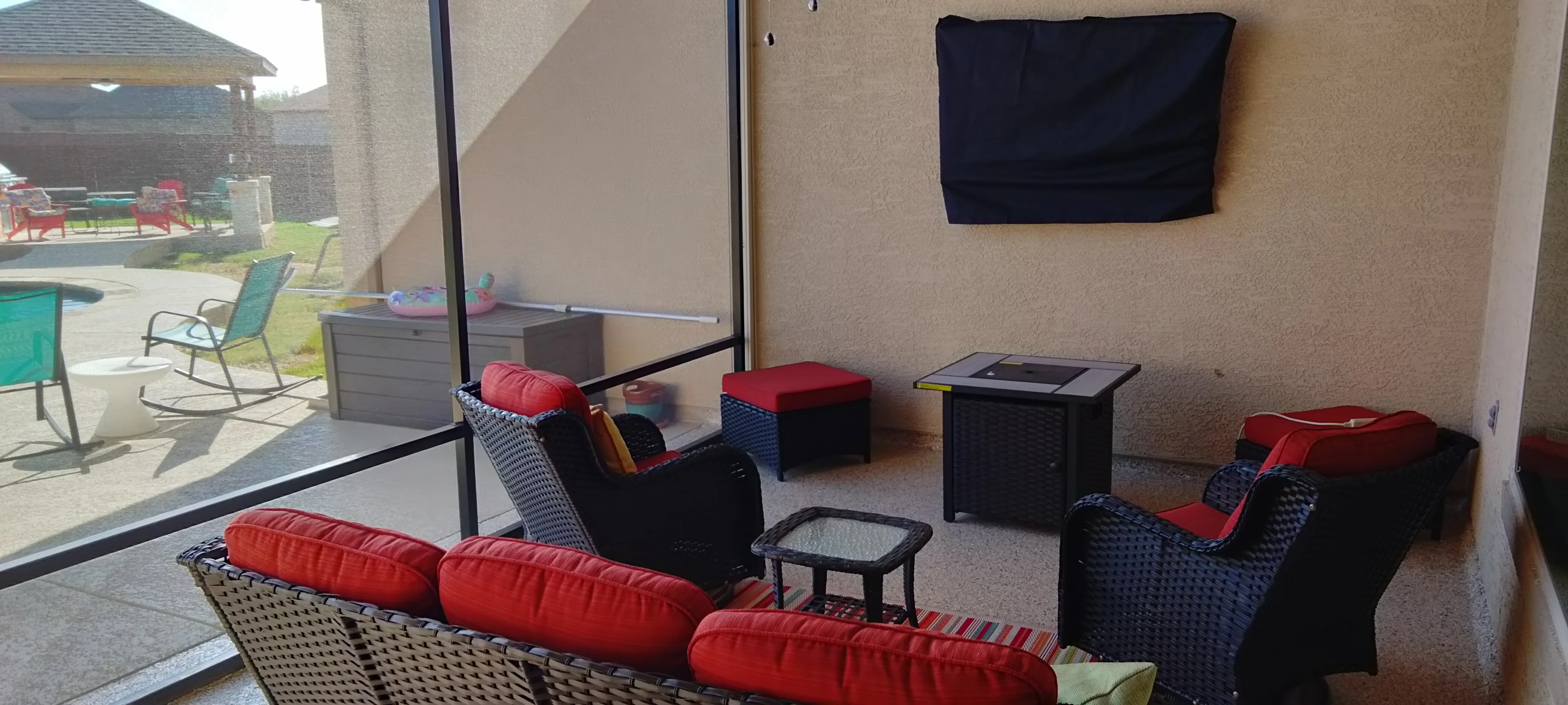 Covered patio with stucco walls, glass doors, concrete floor, woven furniture, and mounted TV