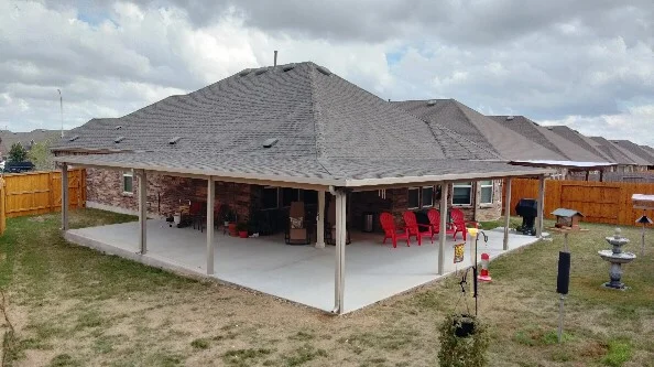 Large covered patio with concrete floor, support columns, and shingled roof attached to residential home