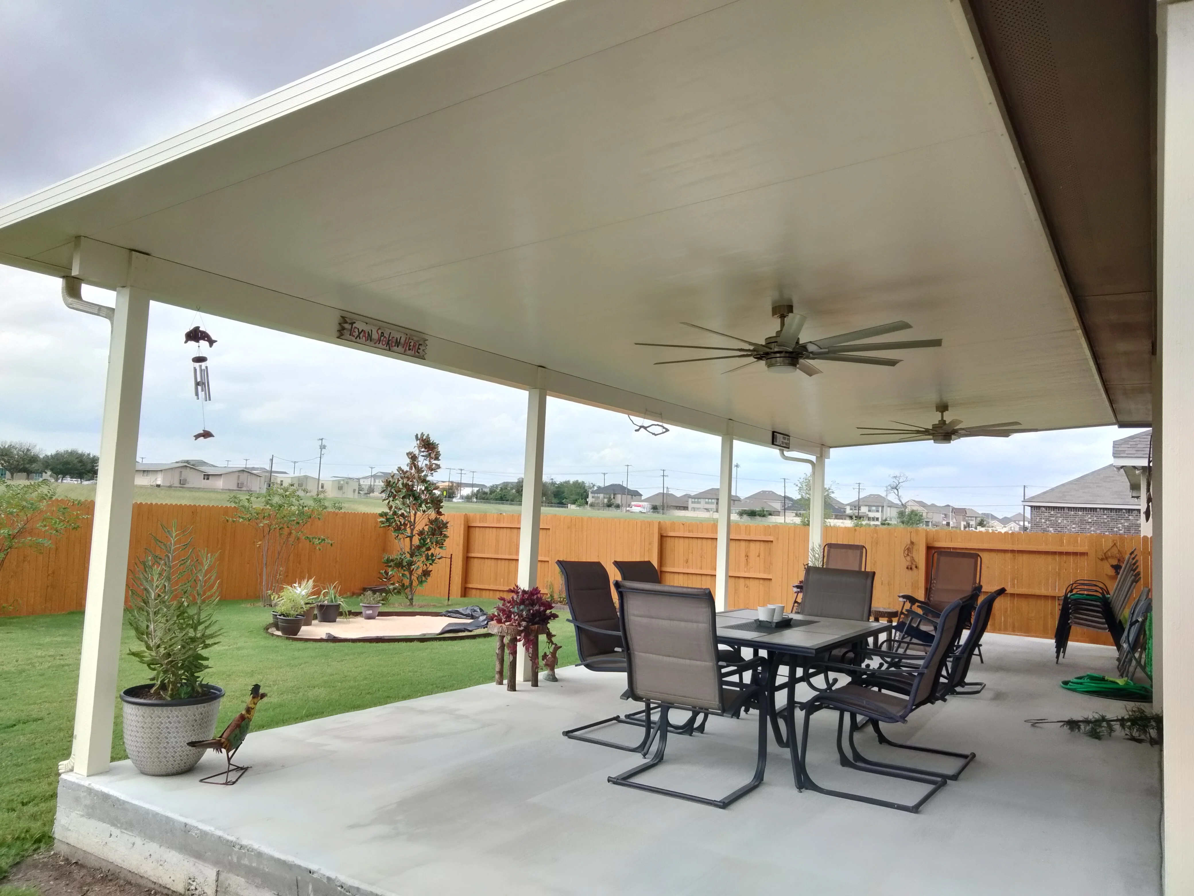 White insulated patio cover with ceiling fans over concrete pad and seating area