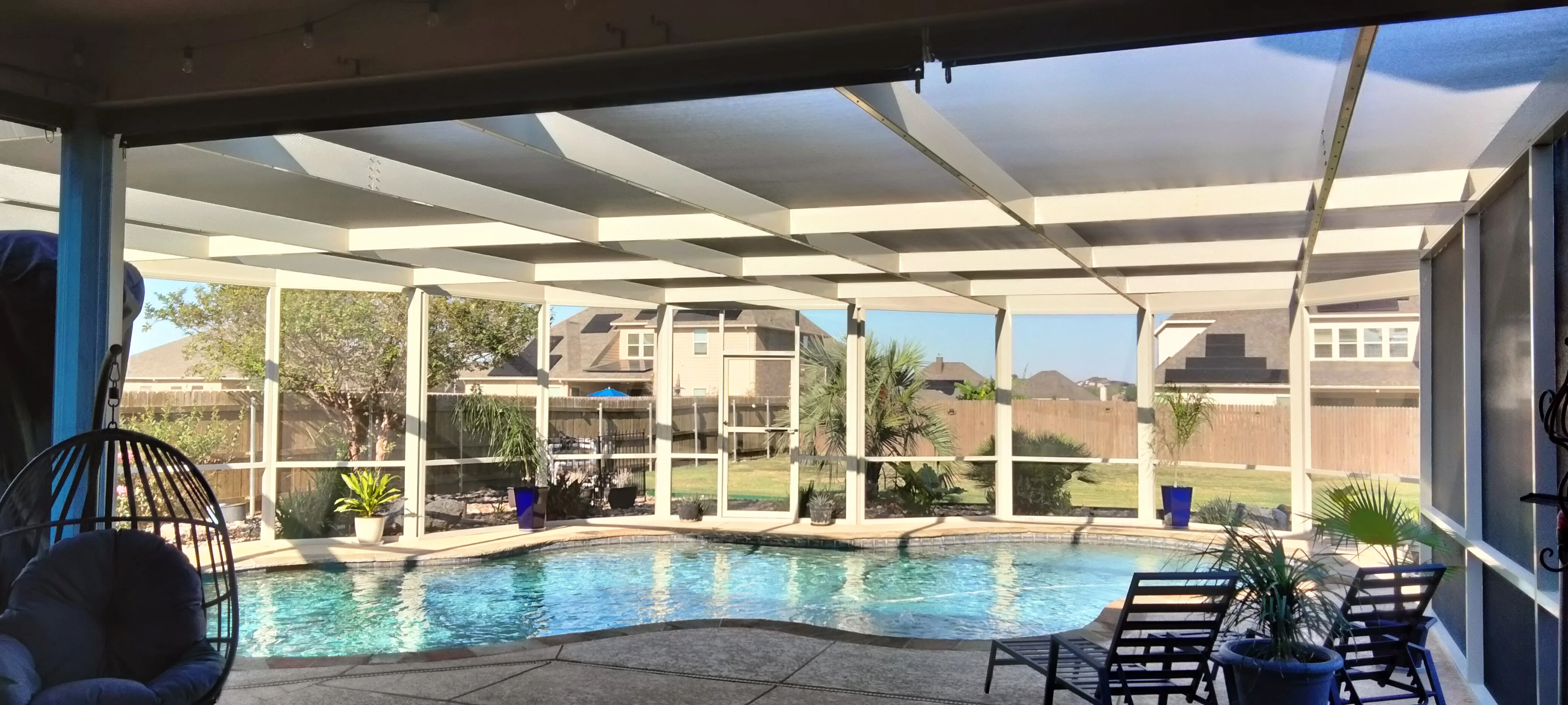 Retractable patio enclosure with motorized shade panels over swimming pool, white aluminum frame and glass panels
