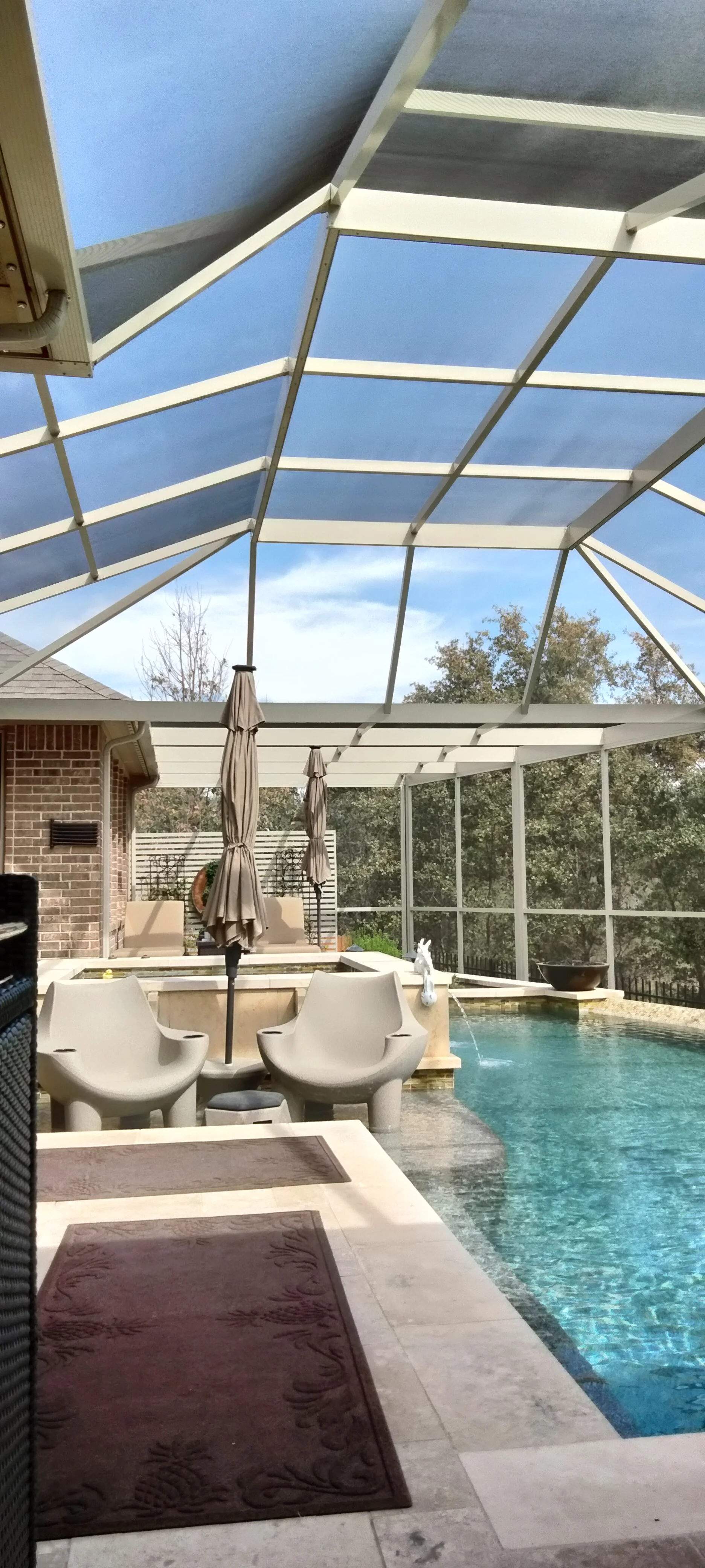 Aluminum pool enclosure with polycarbonate roof panels, screening, and lounge seating