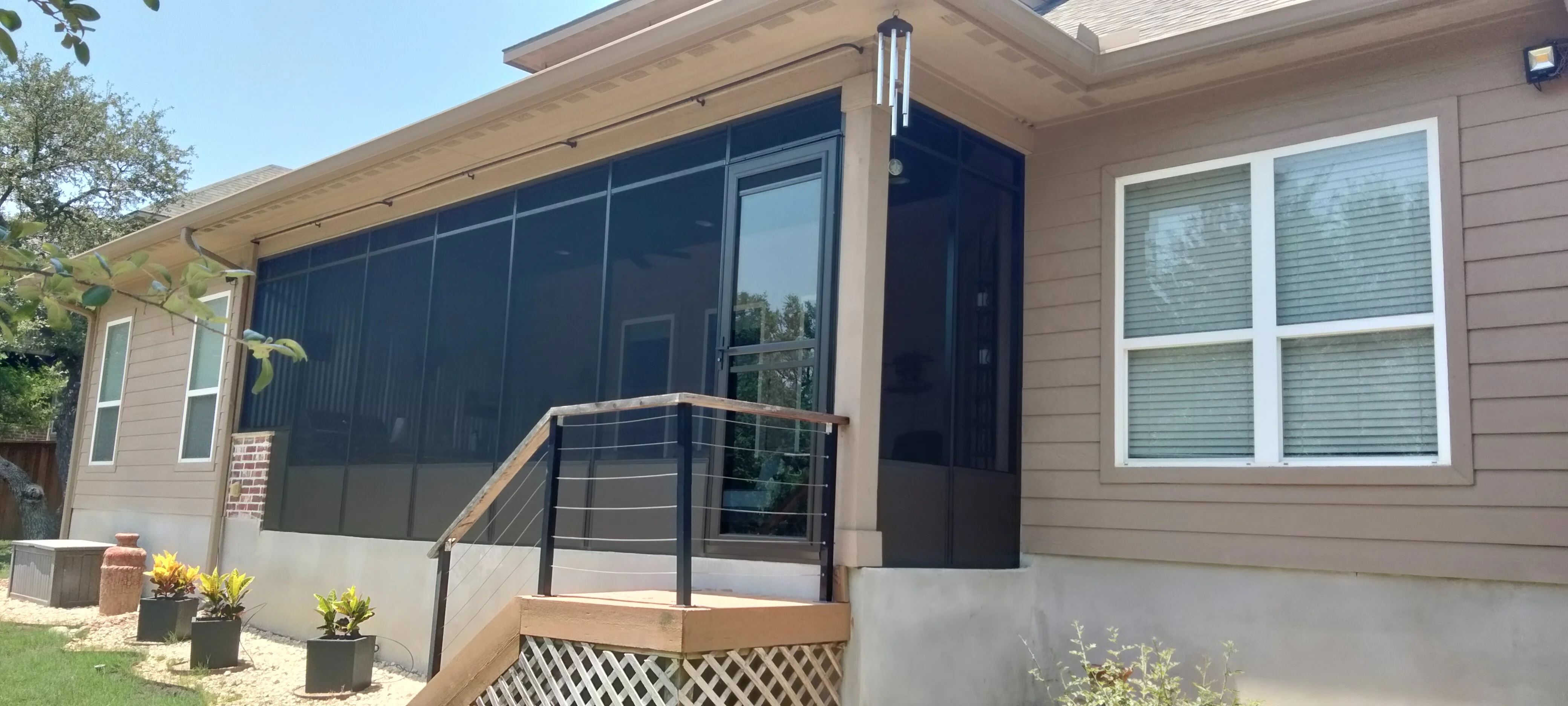 Glass patio enclosure with dark tinted panels, aluminum frame, composite deck, and cable railing