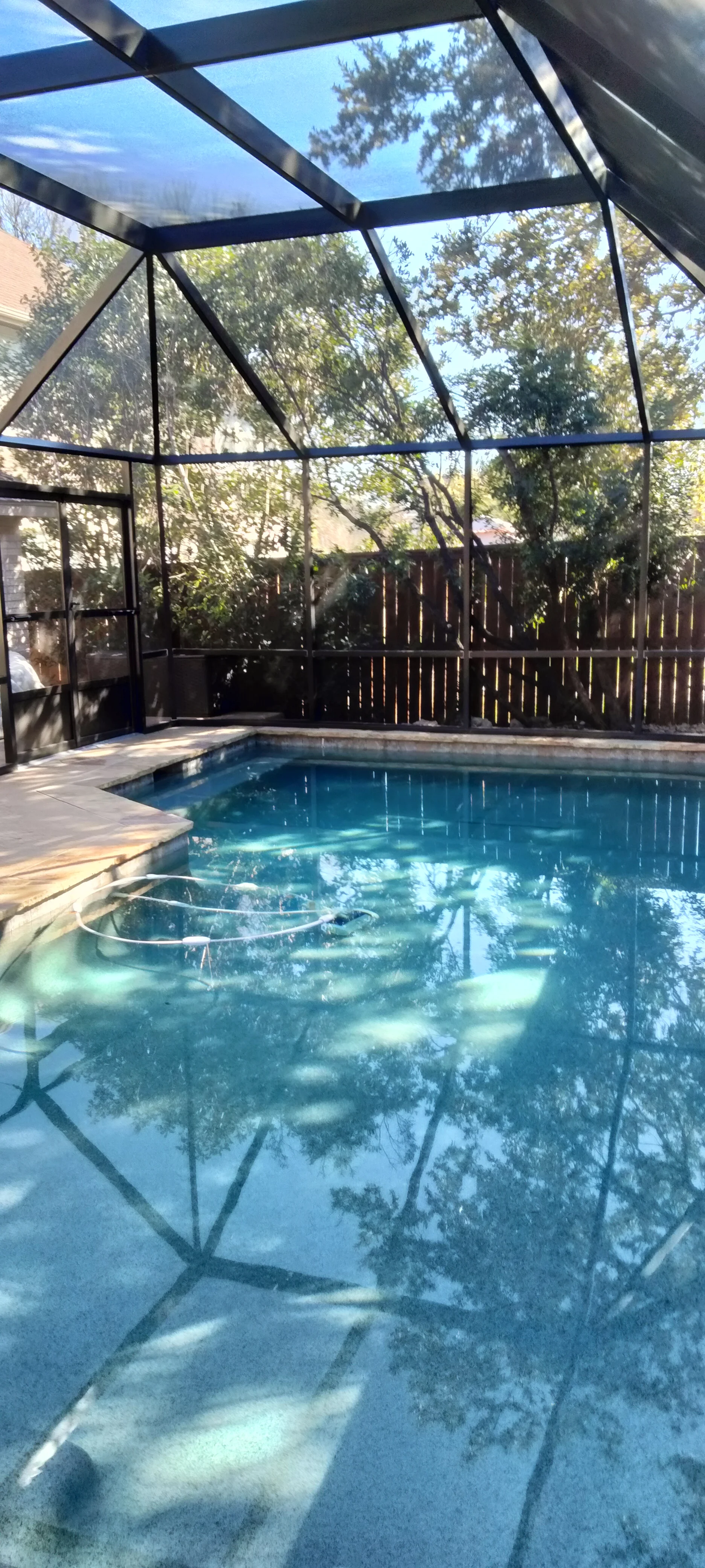 Aluminum-framed pool enclosure with clear panels, gabled roof, and black screening over in-ground pool