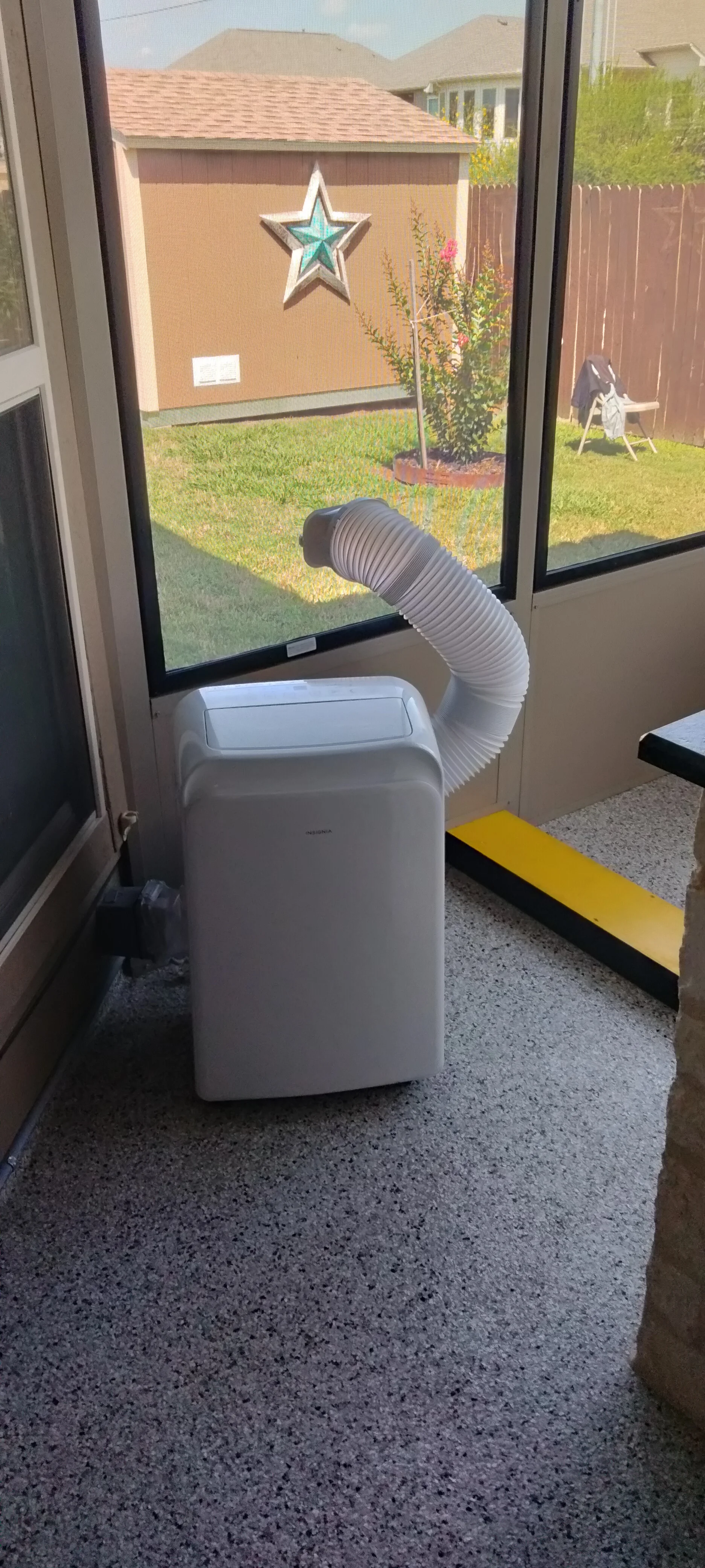 Patio enclosure interior with concrete floor, glass doors, and portable AC unit with ductwork