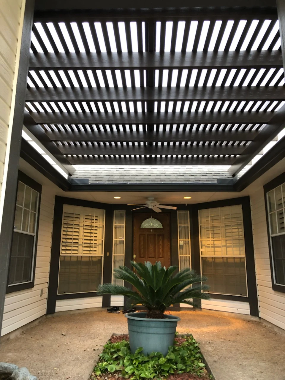 Black aluminum pergola with horizontal solar screen louvers over patio enclosure with glass doors