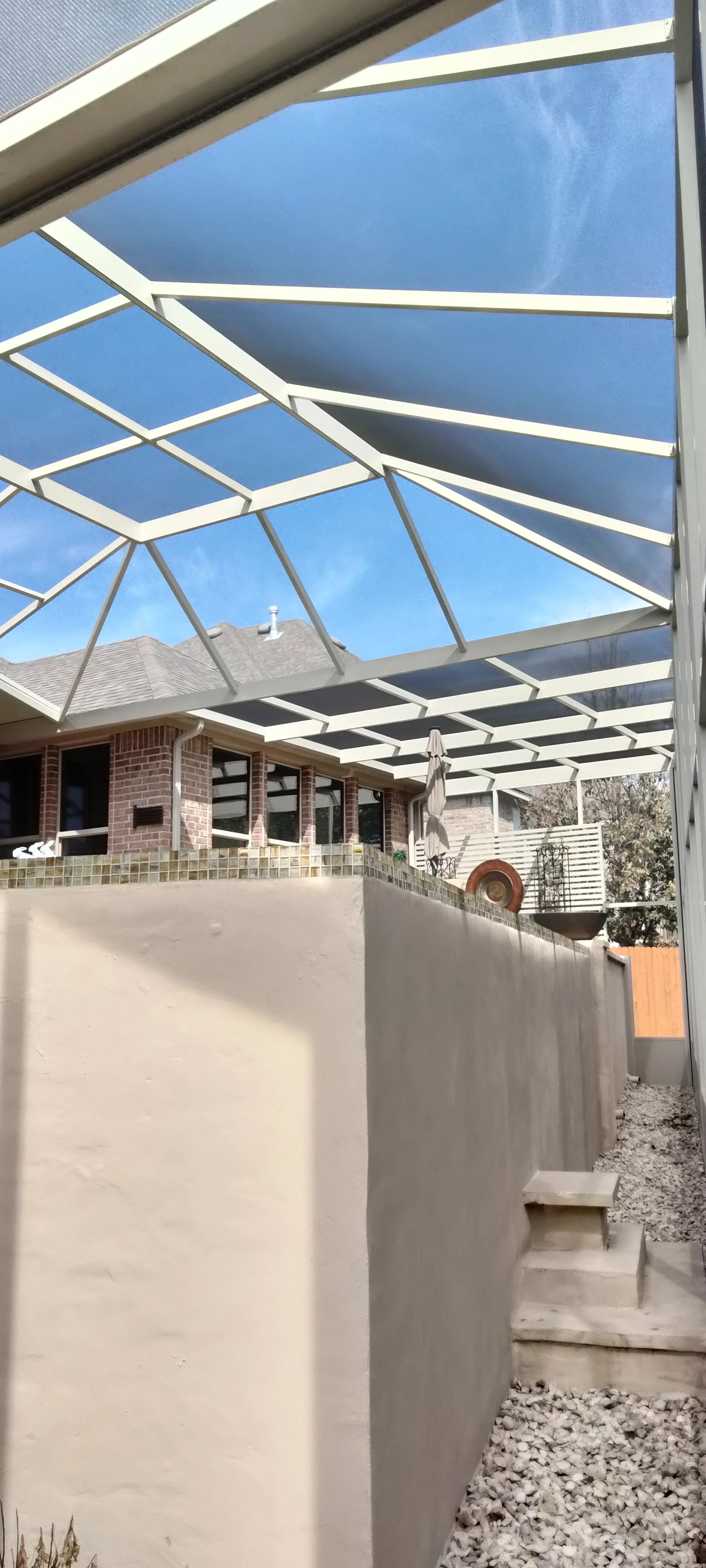 Aluminum patio enclosure with geometric lattice roof and shade louvers over concrete patio