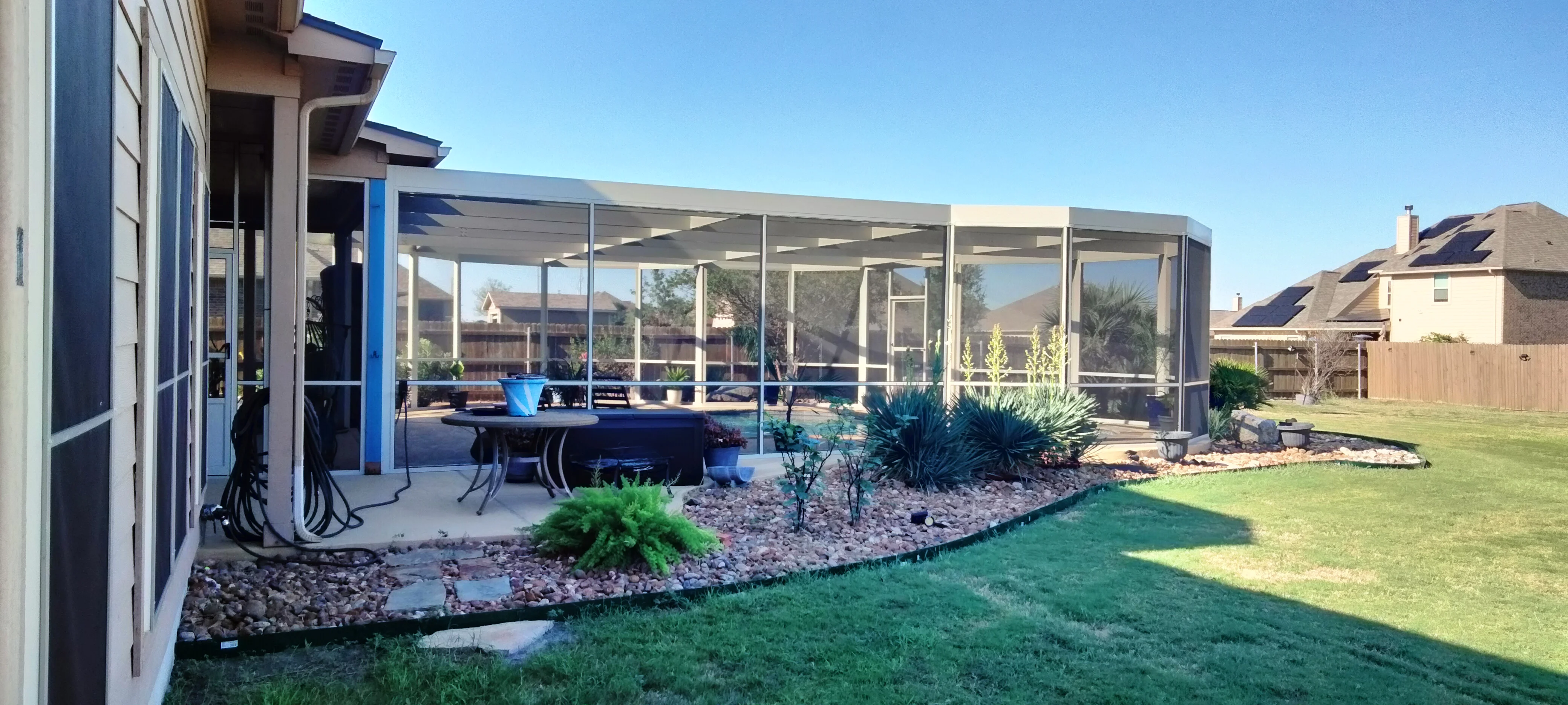 Aluminum patio enclosure with glass panels, shade louvers, and landscaped yard