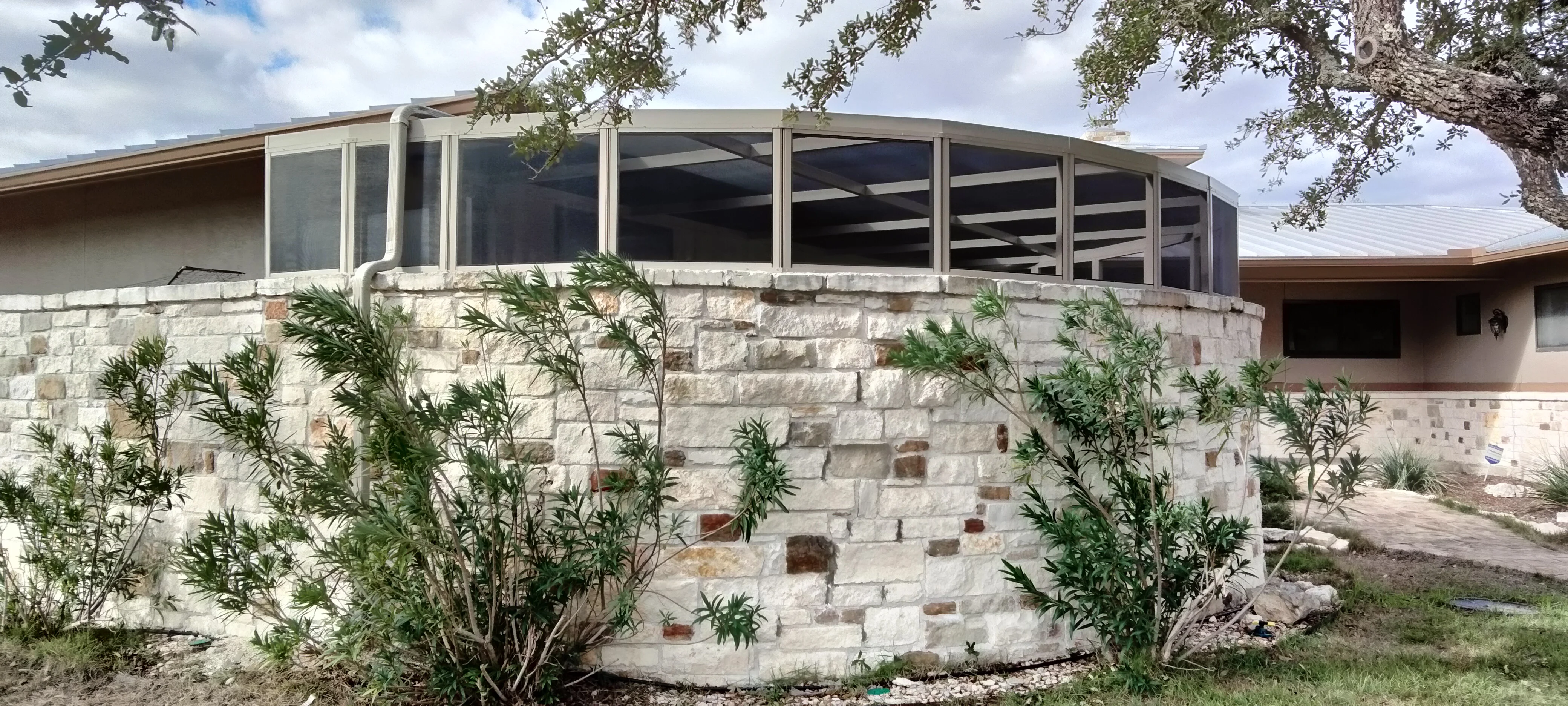 Stone patio enclosure with aluminum frame, glass panels, and metal roof system