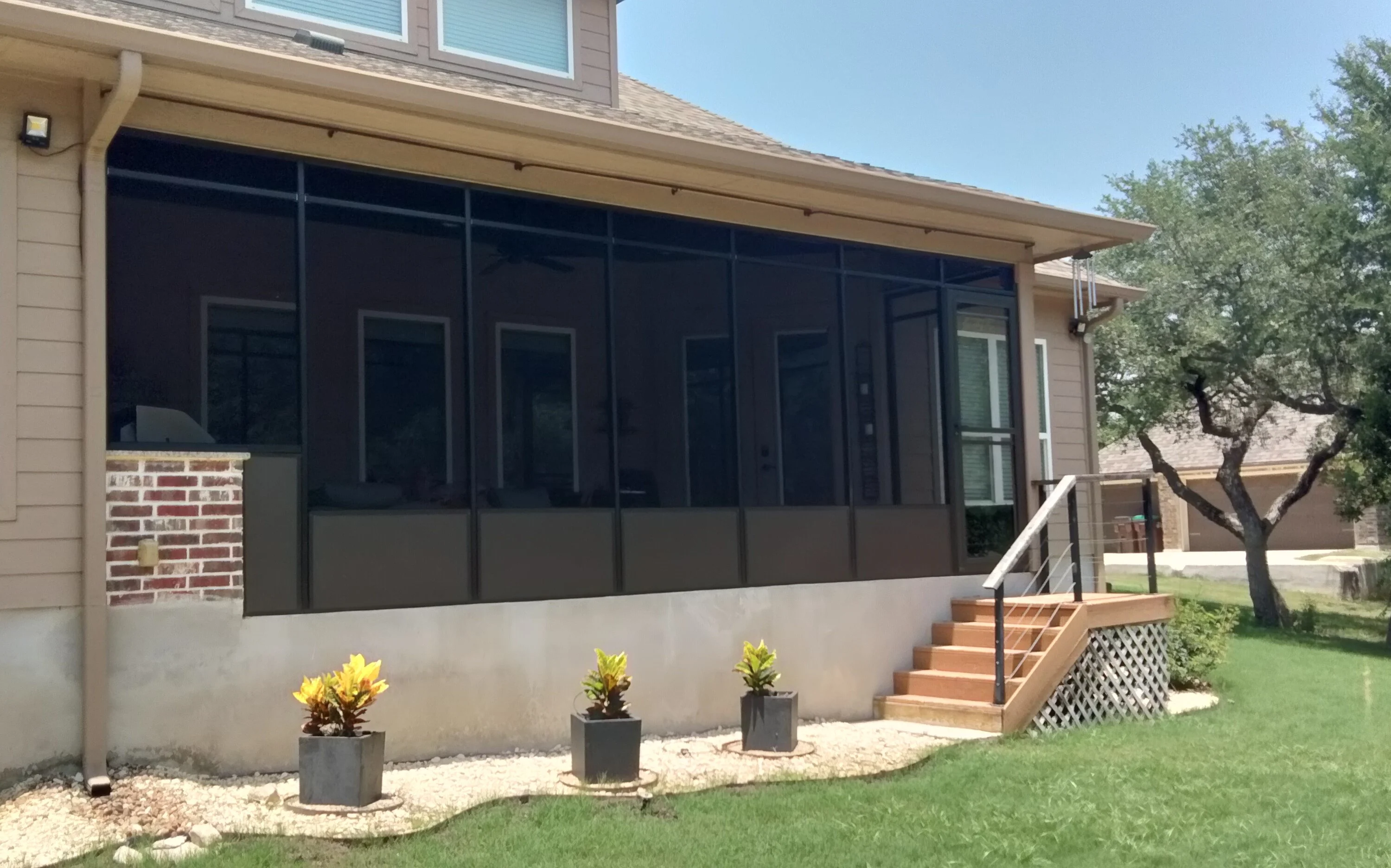 Black-framed patio enclosure with composite deck, metal railings, and tan panel base on residential home