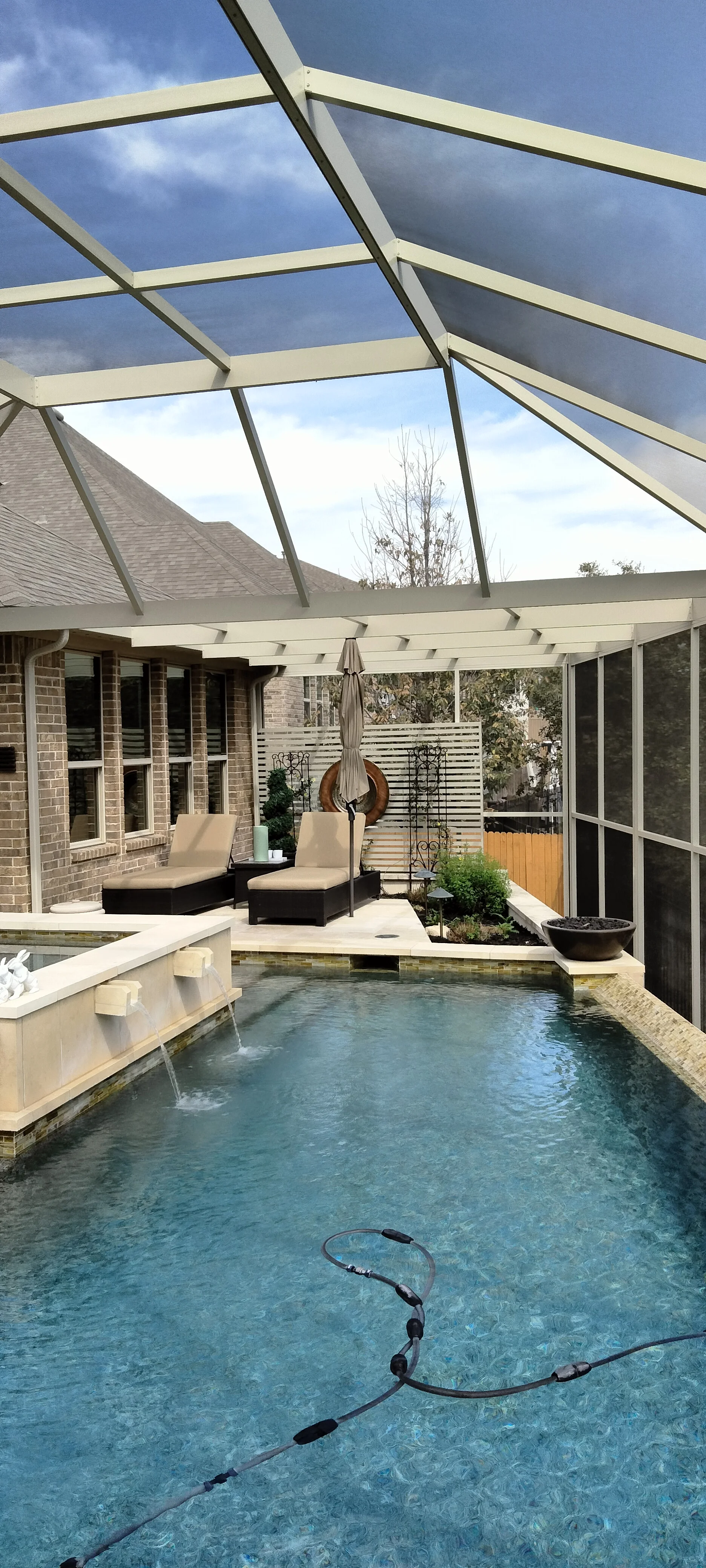 Clear polycarbonate pool enclosure with aluminum frame, lounge chairs, and brick patio surround